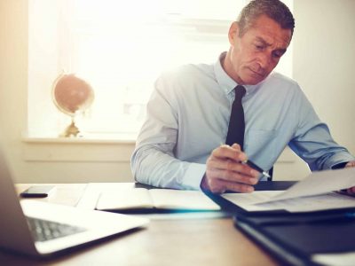 Focused mature businessman wearing a shirt and tie reading through paperwork while sitting at his desk in an office
